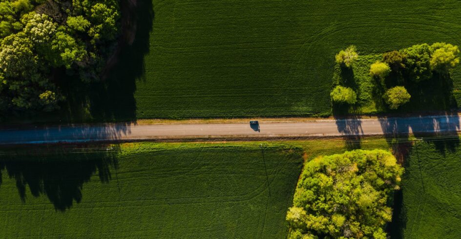 Aerial shot of a car driving on a tranquil road through lush green countryside on a sunny day.